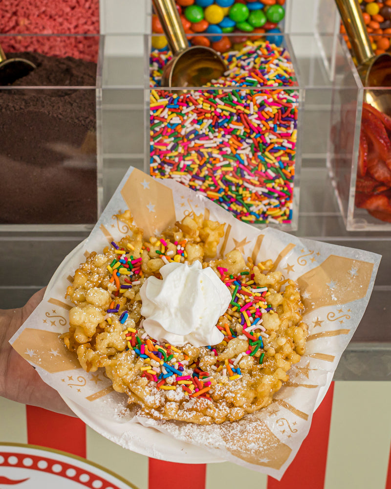 Funnel Cakes closeup with toppings like powdered sugar, whipped cream and rainbow sprinkles